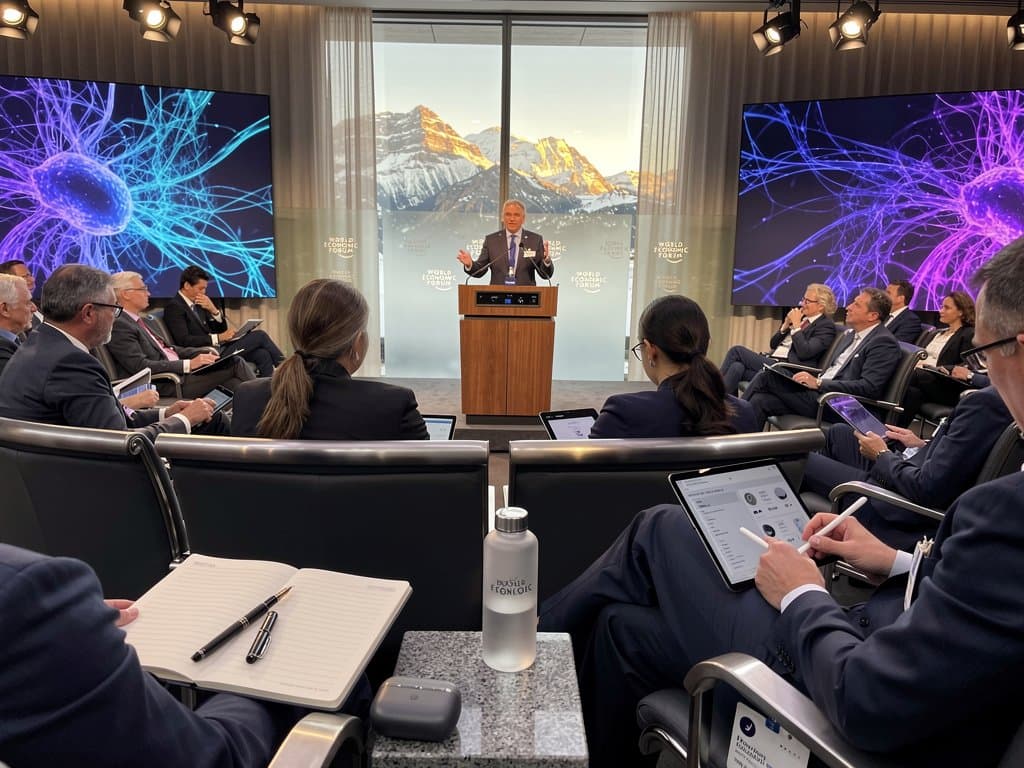 CEO spricht auf WEF-Bühne mit AI-Grafiken, Publikum von Executives in modernem Auditorium mit LED-Lichtern